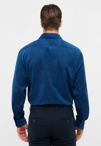 Camicia di cotone blu a maniche lunghe con colletto button-down, texture liscia e polsini con un bottone. La vista posteriore rivela un design dritto.