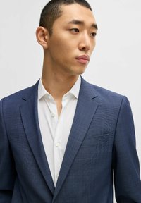 Blazer mit blauem Muster und einem hellen Hemd darunter, ausgestattet mit einem Reverskragen, einer einzelnen Brusttasche und strukturiertem Stoff.