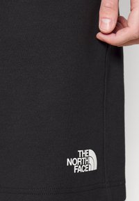 Shorts en coton noir avec une texture lisse et des détails de couture latérale. Présentent un logo brodé blanc "The North Face" près de l'ourlet.