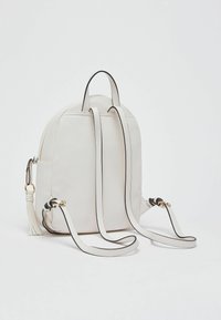 Sac à dos en similicuir blanc avec une forme arrondie, des bordures noires contrastantes, des bretelles ajustables et un pendentif à pampille sur un côté.