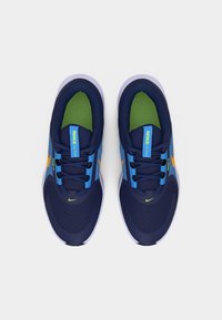 Ζευγάρι από μπλε και ανοιχτό μπλε παπούτσια τρεξίματος Nike με πράσινες εσωτερικές σόλες και πορτοκαλί λογότυπα Swoosh, που φαίνονται από πάνω σε λευκό φόντο.