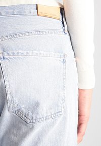 Světle modré džíny z denimu s jednou zadní kapsou, s koženou štítkem v barvě tan s nápisem "Premium Vintage" a viditelnými švy.