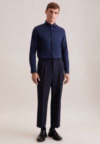 Camicia navy con bottoni, dal tessuto liscio, abbinata a pantaloni navy su misura. Scarpe nere completano l'outfit. Design semplice e minimalista.