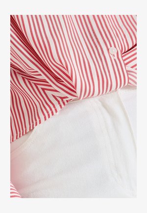 Camisa a rayas rojas y blancas con cierre de botón, superpuesta sobre unos pantalones de mezclilla blancos, que muestran una tela suave y ligera.