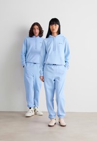 Sudaderas con capucha y pantalones deportivos en azul claro, con puños elásticos. Las sudaderas cuentan con cordones y un bolsillo frontal, mientras que los pantalones deportivos tienen una cinturilla elástica.