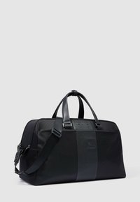 Bolsa de viaje negra con tejido texturizado y detalles de cuero liso. Cuenta con asas dobles, correa ajustable y cierre con cremallera.