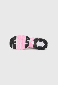 Semelle de chaussure de sport avec un motif en caoutchouc noir texturé, agrémenté de touches de rose et de blanc. Des éléments de rembourrage notables sont visibles.