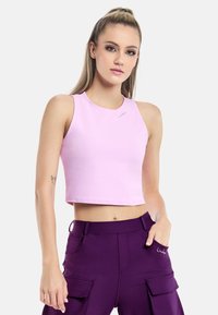 Roosa lühike tank top ümmarguse kaelusega ja ilma varrukateta; sile tekstuur; kantud kõrge vöökohaga lillade laevakottide pükstega, millel on taskud.
