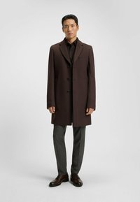 Brown wool coat with a tailored fit, single-breasted design, black buttons, and a chest pocket, paired with gray textured trousers and brown shoes.