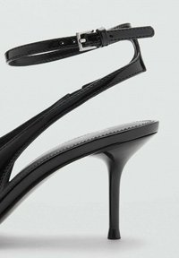 Čierne lakované kožené sandále na vysokom podpätku s úzkym remienkom okolo členku, otvorenou špičkou a elegantným stiletto podpätkom.