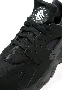 Svart Nike Air Huarache-sneaker med en strukturerad tygövre, perforerad design, tjocka snören och en präglad logotyp på tungan.