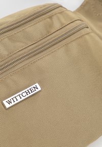 Pochette di tessuto beige con superficie testurizzata, dotata di due scomparti con zip e un'etichetta bianca con la scritta "WITTCHEN."