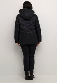 Black padded jacket with a chevron design, featuring a hood and long sleeves, paired with dark slim jeans and black footwear.