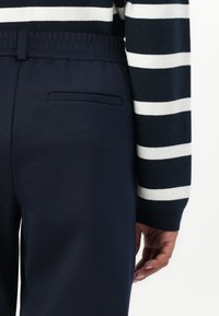Marinebukser med myk tekstur, elastisk midje, med en enkelt baklomme, sammen med en stripete genser i marine og hvitt.