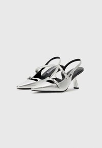 Sølvmetalliske slingback hæler med spiss tå, med en buckle detalj og en slank, skrå hæl. Glatt tekstur og minimalistisk design.