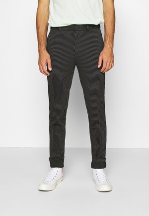 Pantalon noir à rayures fines avec une coupe slim, doté d'un bouton de fermeture, de passants de ceinture et de manches retroussées, associé à des baskets blanches.