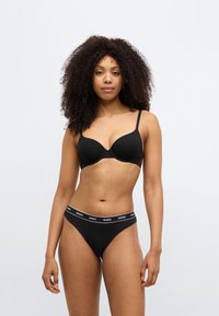 Fekete párnázott melltartó állítható pántokkal, kis piros logóval. Fekete tangabugyi "HUGO" feliratos derékpánttal. Simább anyagtextúra.