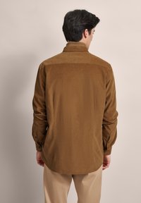 Braunes Langarmhemd aus weichem Stoff mit Kragen, Knopfmanschetten und geradem Saum, von hinten betrachtet.