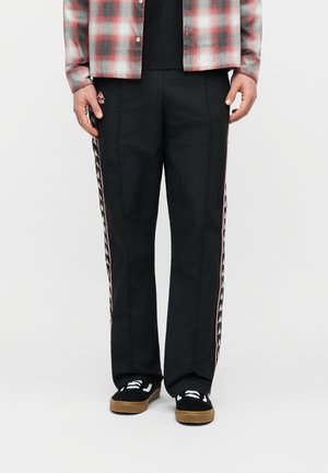 Mees kannab musti spordipükse, mille külgedel on valge ja roosa logoga triibud, ning musti tossusid, millel on valged nöörid ja kummist tallad.