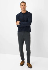 Marineblauwe polo met lange mouwen, gecombineerd met grijze geprägde broek en bruine veterschoenen. Casual outfit met een aansluitende pasvorm en een gladde textuur.