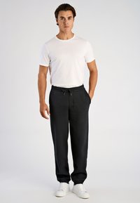 Zwarte joggingbroek met elastische tailleband en trekkoord, voorzien van zijzakken, gecombineerd met een eenvoudig wit T-shirt en witte sneakers.