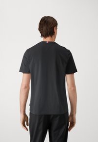 Camiseta negra de manga corta hecha de algodón con escote redondo, que presenta un pequeño acento en rojo, blanco y azul en la parte posterior del cuello.