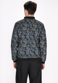 Herre bomberjakke i sort med et blomsterdesign i blå og beige. Har ribbede mansjetter og kant, samt et glat, struktureret stof.