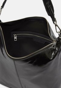Czarna skórzana torebka o błyszczącej powierzchni. Wewnątrz znajduje się kieszeń na zamek błyskawiczny oraz podszewka z tkaniny. Zawiera odłączany pasek i metalowe okucia.
