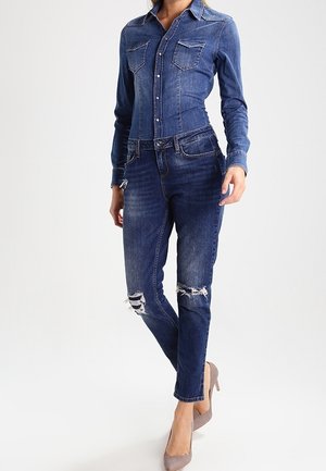 Jeansowa koszula i przetarte dżinsy w ciemnym niebieskim kolorze. Posiada zapięcie na guziki, dwie kieszenie na piersi oraz lekko postrzępiony detal na kolanie. Noszone z beżowymi szpilkami.