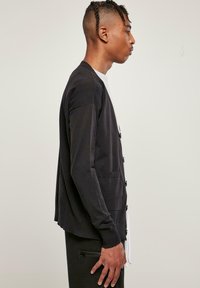 Fekete kardigán puha anyagból, hosszú ujjakkal, gombos elülső résszel és két elülső zsebbel. Sima textúra, laza fit.