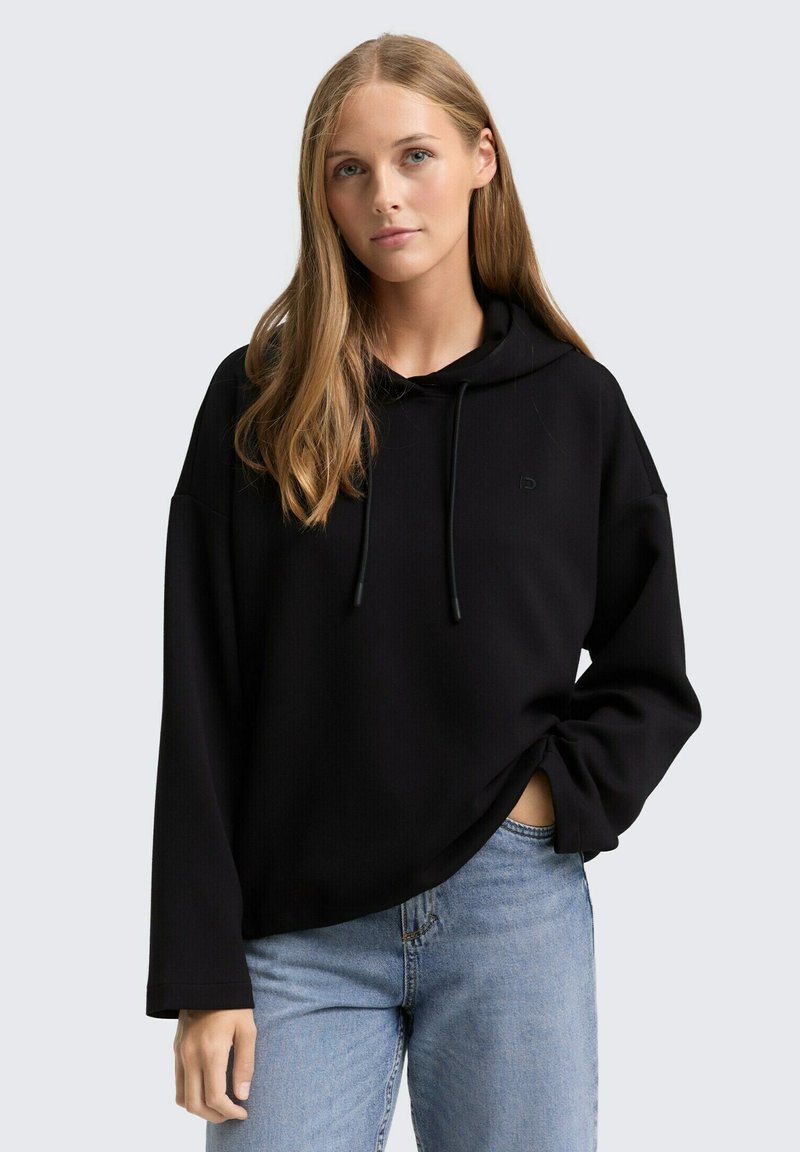 Zwarte hoodie met lange mouwen, trekkoorddetails en een relaxed fit. Gecombineerd met lichtblauwe jeans, met een subtiel logo.