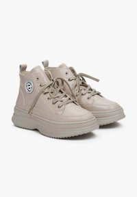 Mid-top sneakers in light beige leather, featuring round logo, lace-up design, textured rubber sole, and stitching details along edges.