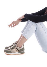 Zapatillas con estampado de leopardo y detalles en verde oliva y dorado metálico, con un upper texturizado, cierre de cordones y suela de goma, exhibidas con jeans claros.