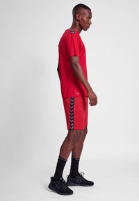 Camiseta atlética roja y pantalones cortos con acentos de chevron negros, hechos de una tela ligera. Llevado con zapatos atléticos negros y calcetines.