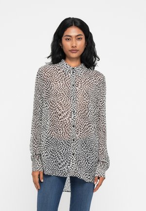 Camicia a bottoni nera e bianca trasparente con motivo astratto, maniche lunghe e colletto a punta. Abbinata a jeans in denim blu.