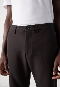 Black trousers made of smooth fabric, featuring a button closure, front pockets, and a slim fit design. Worn with a white t-shirt.