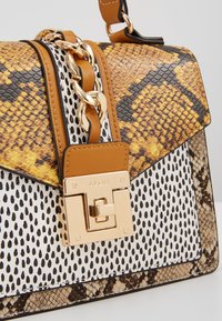 Rakennettu käsilaukku, jossa on keltaruskea käärmeprintti, valko-mustalla pilkullisella tekstuurilla, kultaiset yksityiskohdat ja ketjuviimeistely.