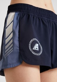 Sotut urheiluhousut, joissa on valkoinen logo, sivupaneeli, jossa on gradienttikuva, joustava vyötärö ja kevyt, hengittävä kangas.