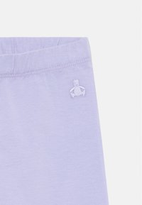 Šviesiai violetiniai medvilniniai šortai su elastinga juostos ir mažo siuvinieto meškinuko logotipu ant šono. Minkšta, lygi tekstūra.
