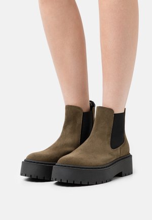 Bottines en suède marron avec des panneaux élastiques latéraux noirs et de épaisses semelles plateforme noires présentant une texture nervurée.