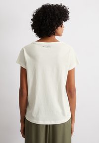 T-shirt en coton blanc à manches courtes, avec un col rond et un logo imprimé dans le haut du dos. Texture douce et coupe décontractée.