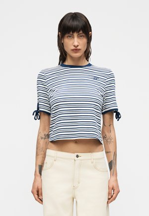 Ριγέ cropped τοπ σε ναυτικό μπλε και λευκό, με κοντά μανίκια και δεσίματα στις μανσέτες. Κατασκευασμένο από ελαφρύ ύφασμα, με άνετη εφαρμογή και στρογγυλή λαιμόκοψη.