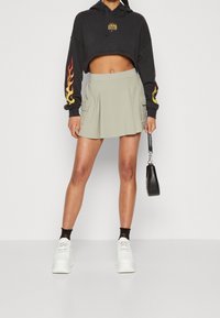 Zkrácená černá mikina s grafikou plamenů, v kombinaci se světle zelenou plisovanou mini sukni s cargo kapsami. Bílé platformové tenisky.