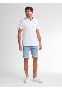 Camisa polo blanca de manga corta y cuello, combinada con pantalones cortos de mezclilla ligeros y enrollados en azul claro y zapatillas beige.