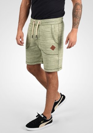 Shorts verts chinés avec taille élastique, fermeture à cordon, poches latérales et patch logo en cuir marron. Tissu en mélange de coton.