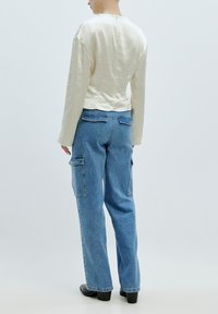 Crèmewitte satijnen top met lange mouwen, gecombineerd met relaxte blauwe denim cargobroek met patch pockets en een hoge taille.