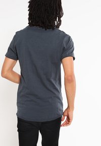 T-shirt à manches courtes gris foncé en tissu doux et texturé, avec un col rond et un ourlet arrière légèrement plus long.