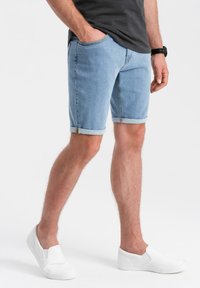 Shorts de mezclilla azul claro con dobladillos enrollados, que cuentan con bolsillos, un diseño sin costuras y detalles de cremallera lateral. Combinados con zapatos blancos tipo slip-on.