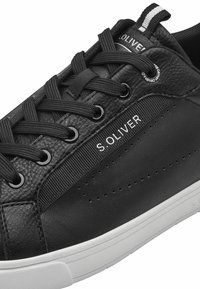 Fekete sneaker, textúrált bőr és sima szintetikus részletekkel, kerek fekete fűzőkkel, perforált részletekkel és fehér talppal.
