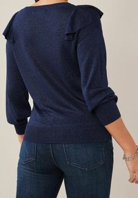 Pull en tricot bleu marine avec des accents de épaules froncés, des poignets côtelés et une coupe structurée. Présente un éclat subtil et une finition texturée.